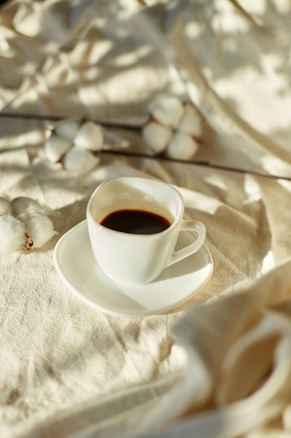 Cup of coffee in bed with cotton flowers morning mood Organic and natural linen cotton textile bedclothes copy space