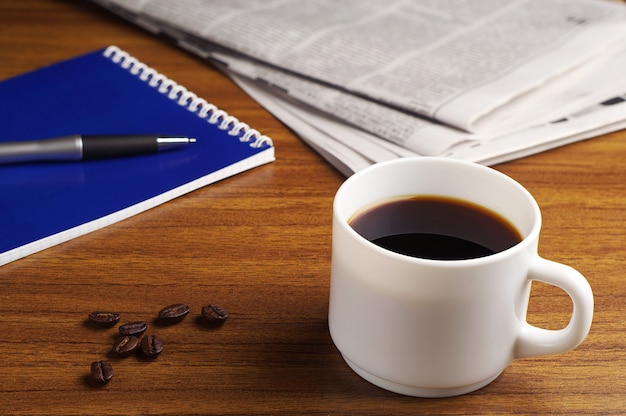 Cup of coffee beside newspaper and notebook