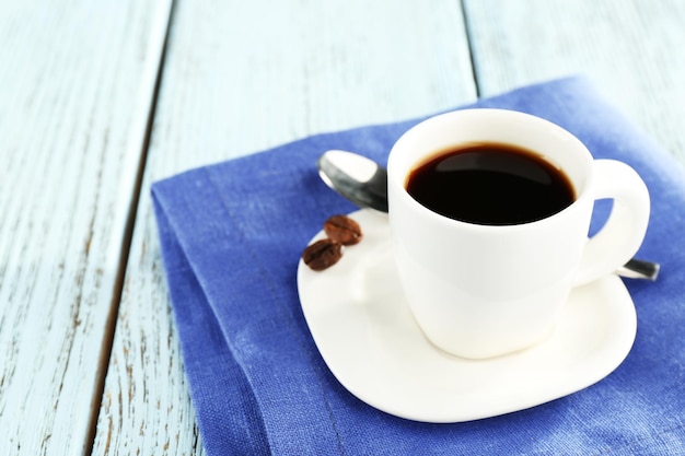 Cup of coffee on blue napkin on color wooden background