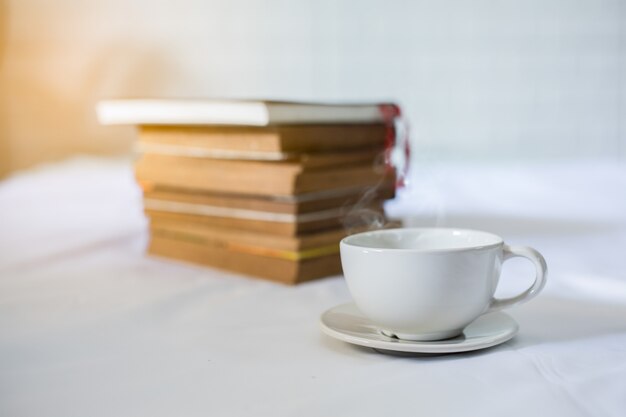 Cup of coffee and a book on a bed. White cup with coffee on a book. Close up