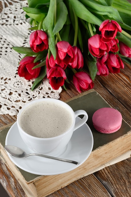 Чашка кофе книга миндальное печенье тюльпаны и вязаная салфетка на деревянном столе