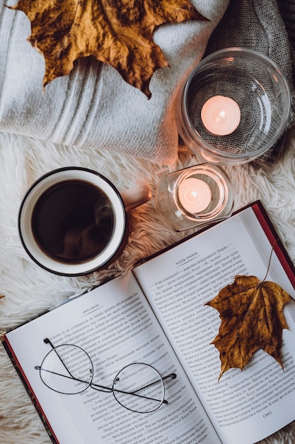 A Cup of coffee, a book on a white blanket, candles, glasses.