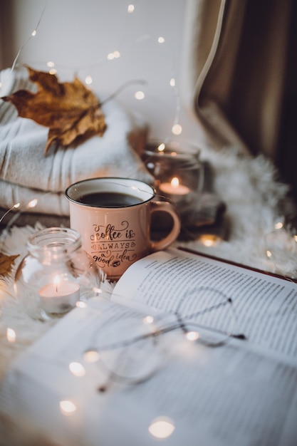 A Cup of coffee, a book on a white blanket, candles, glasses.