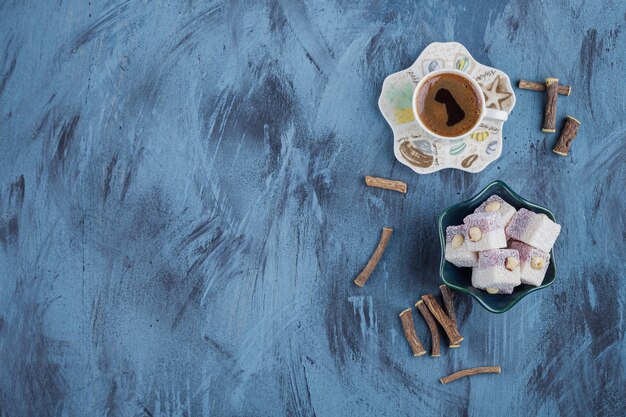 Cup of coffee and bowl of rose delights on blue background. 