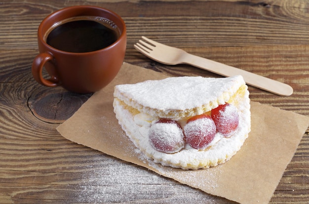 Cup of coffee and cake with grape berries, sprinkled with powdered sugar on old wooden table