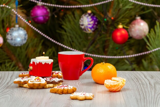 Cup of coffee candle and a fir tree with Christmas ornaments on the background