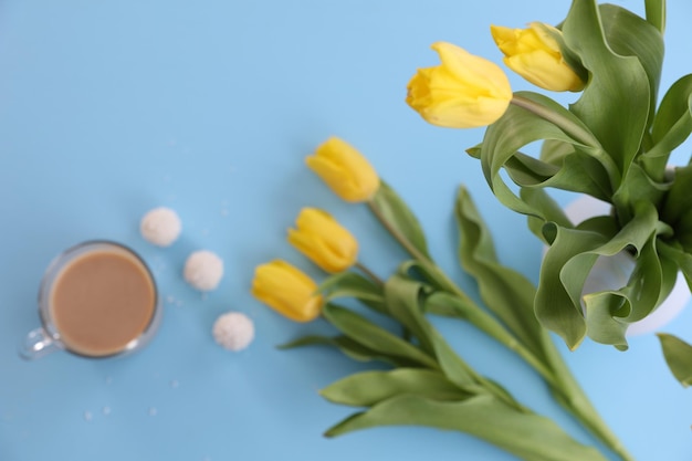 A cup of coffee candy and yellow tulips on a blue background
