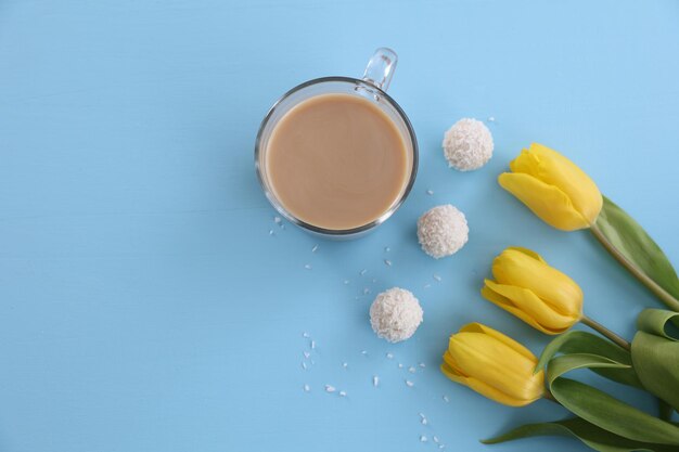 A cup of coffee candy and yellow tulips on a blue background