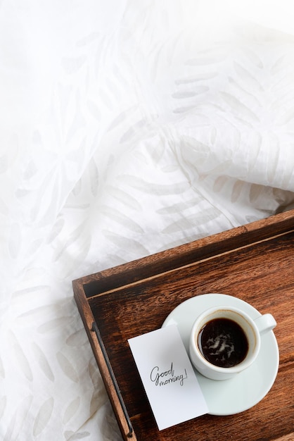 Photo cup of coffee and card with text good morning on wooden tray on a white cozy background