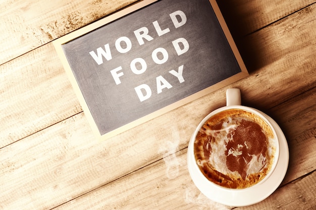 The cup of coffee and chalkboard with World Food Day text on wooden