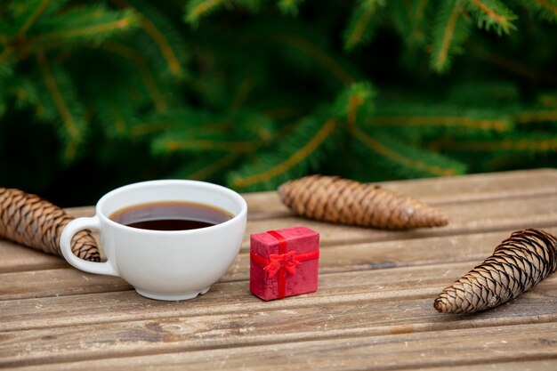 Cup of coffee and Christmas gift on wooden table with spruce branches on background