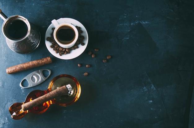 Cup of coffee, coffee beans, ashtray with cigar on dark