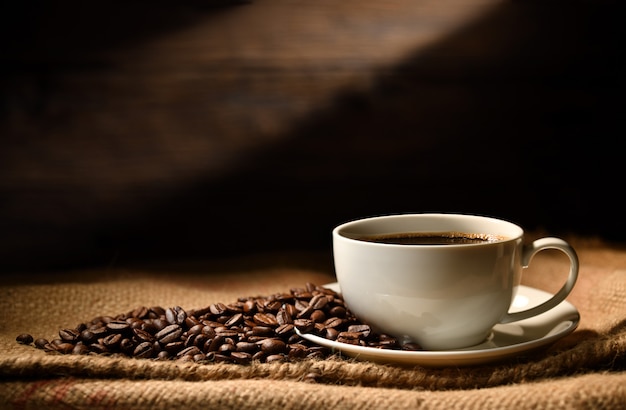 Cup of coffee and coffee beans on burlap sack on old wooden background