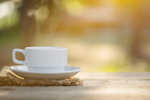 Cup of coffee and coffee beans on outdoor wooden table in morning sunlight and bokeh background