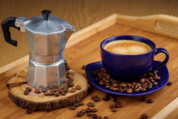 Foto tazza di caffè e chicchi di caffè su un piatto e caffettiera geyser su un vassoio di legno