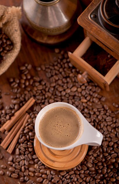 Cup of coffee and coffee beans in a sack on dark surface, top view