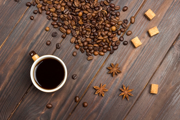 Cup of coffee. Coffee beans scattered on table, star anise and pieces of brown sugar