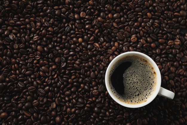 Cup of coffee on coffee beans, top view