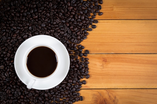 Cup of coffee and coffee beans on wood background, top view.