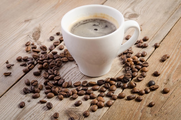 La tazza di caffè e chicchi di caffè sulla tavola di legno