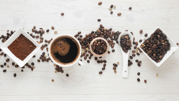Tazza di caffè; caffè in polvere e chicchi di caffè disposti in fila sulla scrivania