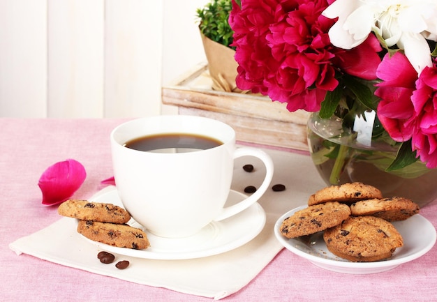 Cup of coffee cookies and flowers on table in cafe