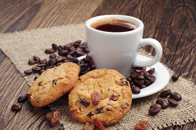 Tazza di caffè e biscotti con uvetta e chicchi di caffè su tessuto ruvido