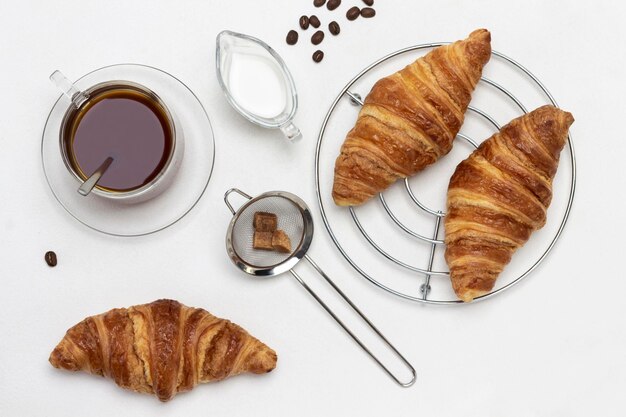 Cup of coffee, cream and brown sugar. Croissants on round metal stand. Flat lay. White background.