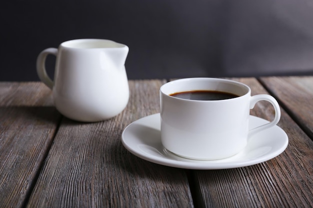 Cup of coffee and cream in milk jug on wooden table on dark background