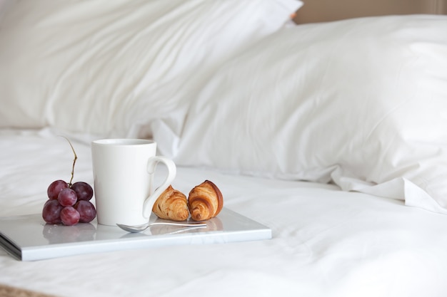 a Cup of coffee and a croissant on a tray on the bed