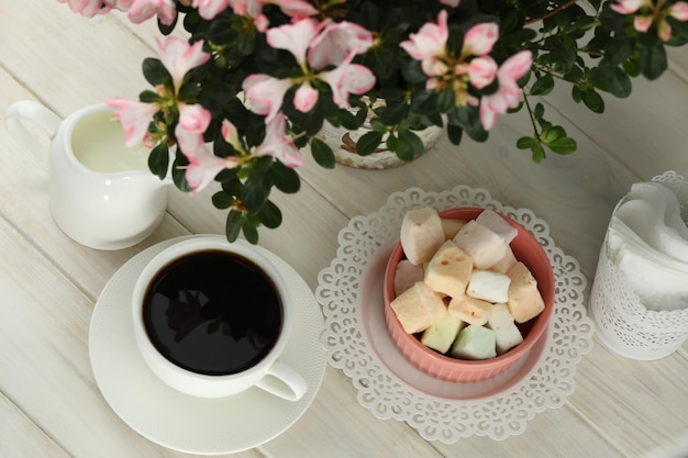 A cup of coffee and a cup of coffee sit on a table next to a plant with flowers.