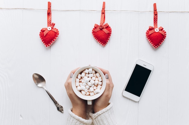 A cup of coffee, decorative hearts, gifts and smartphone on a white table for valentine's 