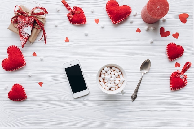 Una tazza di caffè, cuori decorativi, regali e smartphone su un tavolo bianco