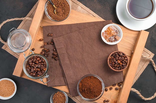 A cup of coffee, different types of coffee and sugar in cups on a brown wall. Top view with copy space.