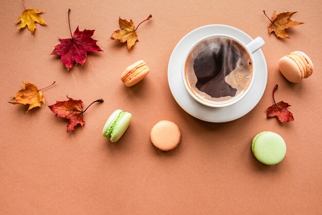 Cup of coffee and dry leaves on brown background. Flat lay, top view, copy space