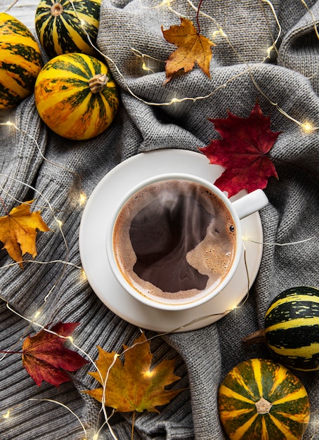 Cup of coffee, dry leaves and scarf on a table.