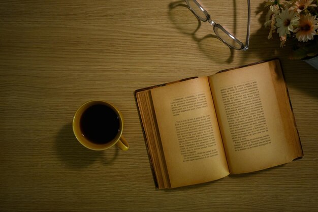 A cup of coffee eyeglasses and open book on rustic wooden table Top view with space for text