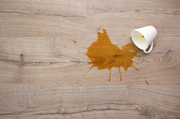 A cup of coffee fell on laminate coffee spilled on floor Focus on the puddle Flat lay Top view