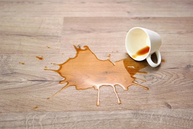 Photo a cup of coffee fell on laminate coffee spilled on floor focus on the puddle