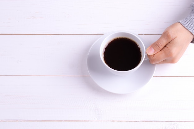 Cup of coffee in female hand on white wooden table