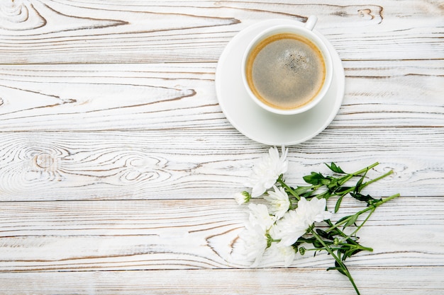 Cup of coffee and flowers on light wooden table