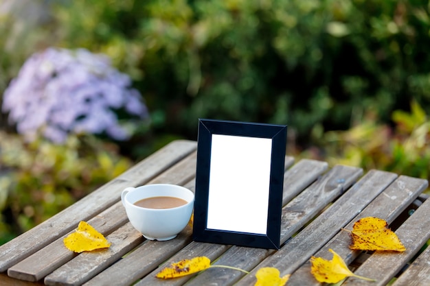 庭のテーブルの上の写真のためのコーヒーとフレームのカップ