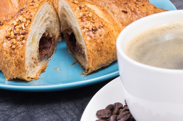 一杯のコーヒーと焼きたてのクロワッサンと朝食用のプレートにチョコレート