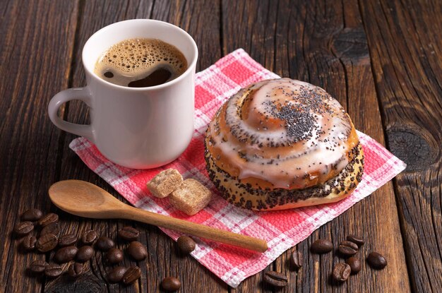 Cup of coffee and fresh sweet bun with poppy seeds on dark wooden table