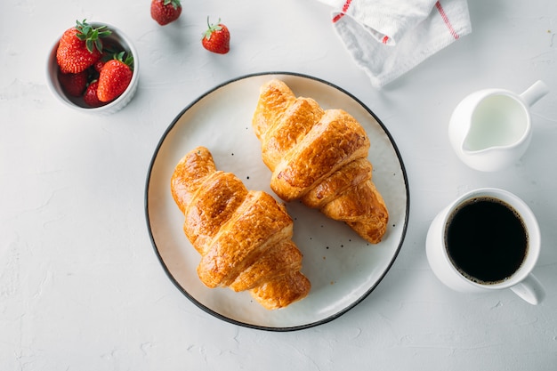 Cup of coffee, freshly baked croissants and fresh strawberry on wooden background