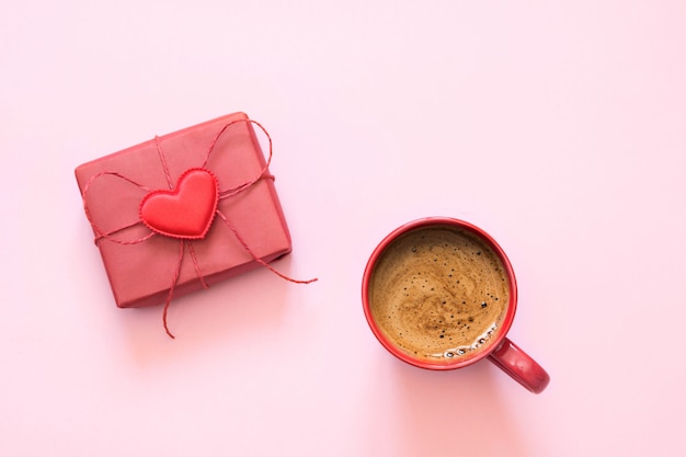 Cup of coffee and gift with love on pastel pink. Top view. Valentine's card.