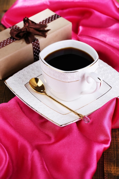 Cup of coffee and gift on wooden table close-up