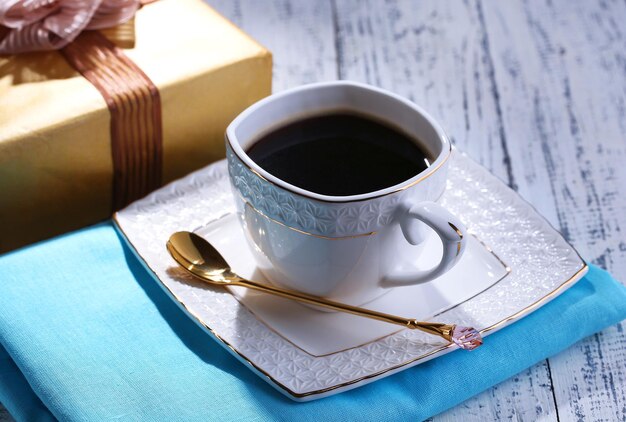 Cup of coffee and gift on wooden table close-up