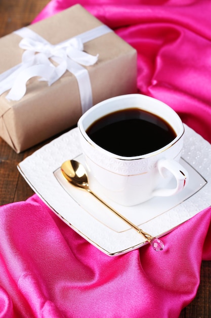 Cup of coffee and gift on wooden table close-up