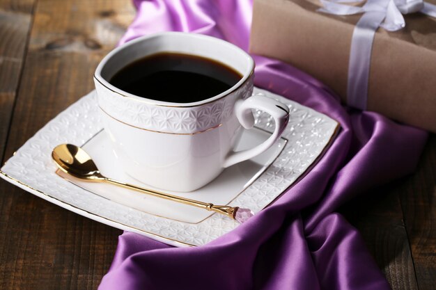 Cup of coffee and gift on wooden table close-up